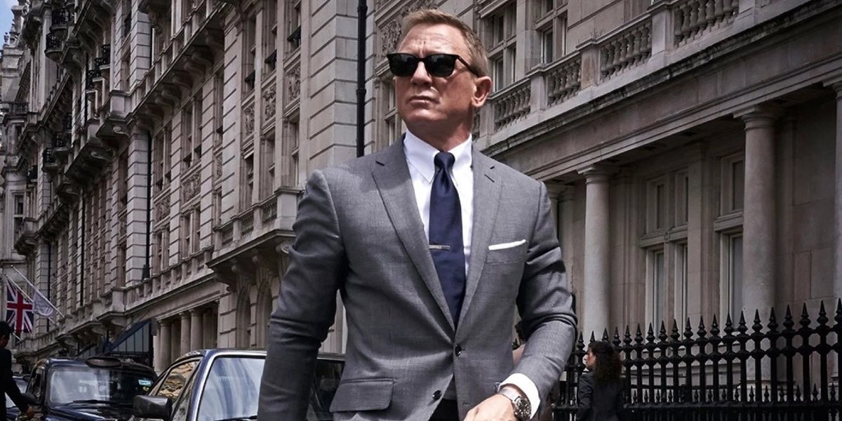 No Time To Die Daniel Craig, in sunglasses, walks down the street wearing a grey suit