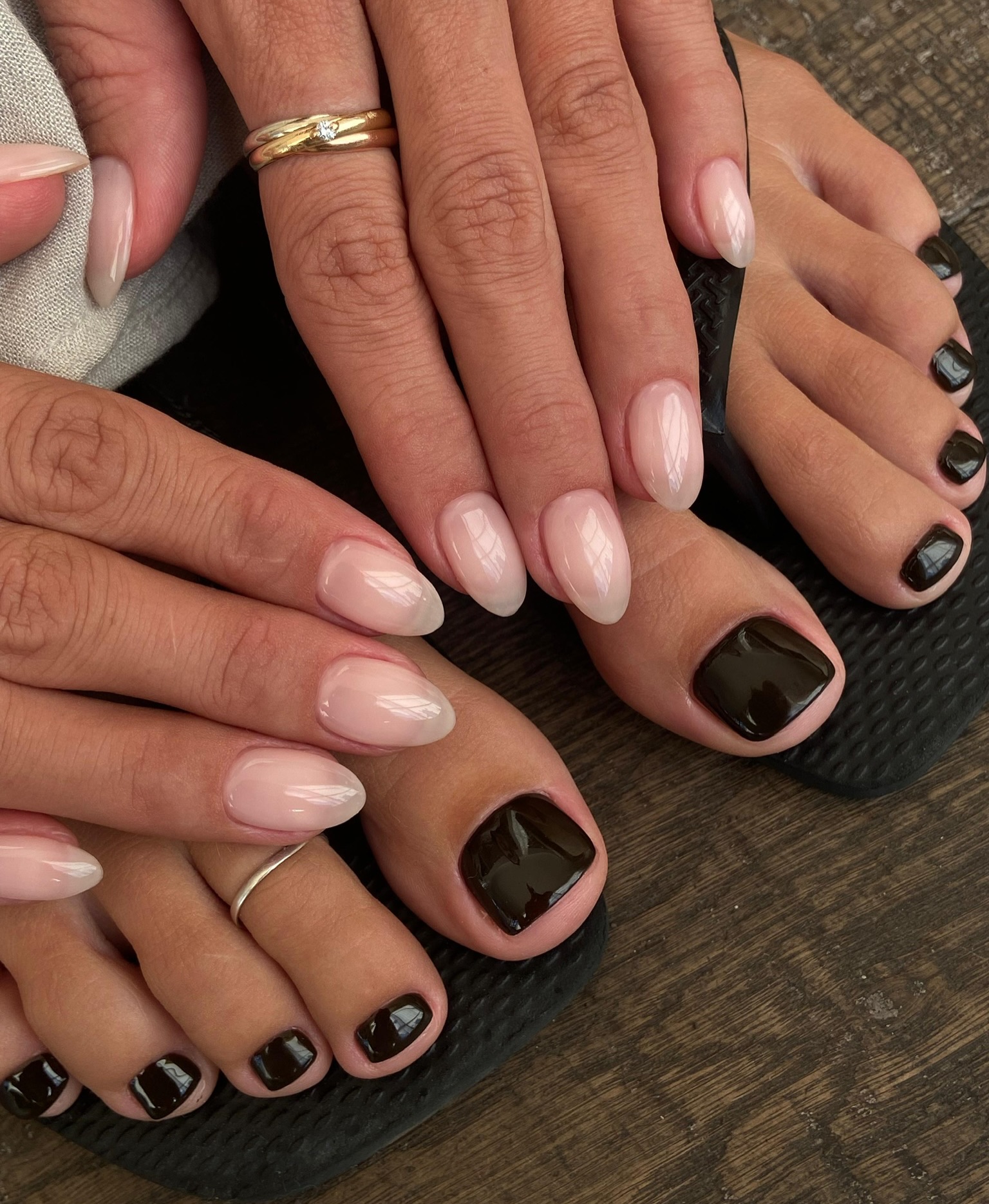 Hands with sheer pale pink almond nails beside toes painted a glossy dark brown-black