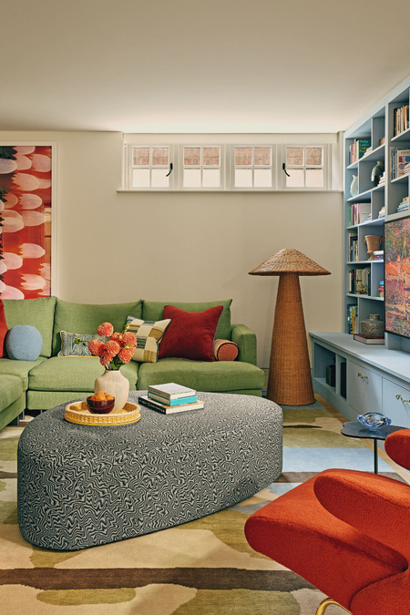 Colorful seating room area featuring a painterly rug, swirl-upholstered irregularly shaped ottoman, and a woven floor lamp 