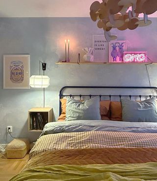 Soft blue wallpaper in small bedroom with soft green and brown patterned bedding and neon lighting