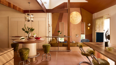 A modern open plan living space with wood and metal accents, a round built-in table with three green stools around it and a large moon-like pendant light about the conversation pit-style seating area at the back