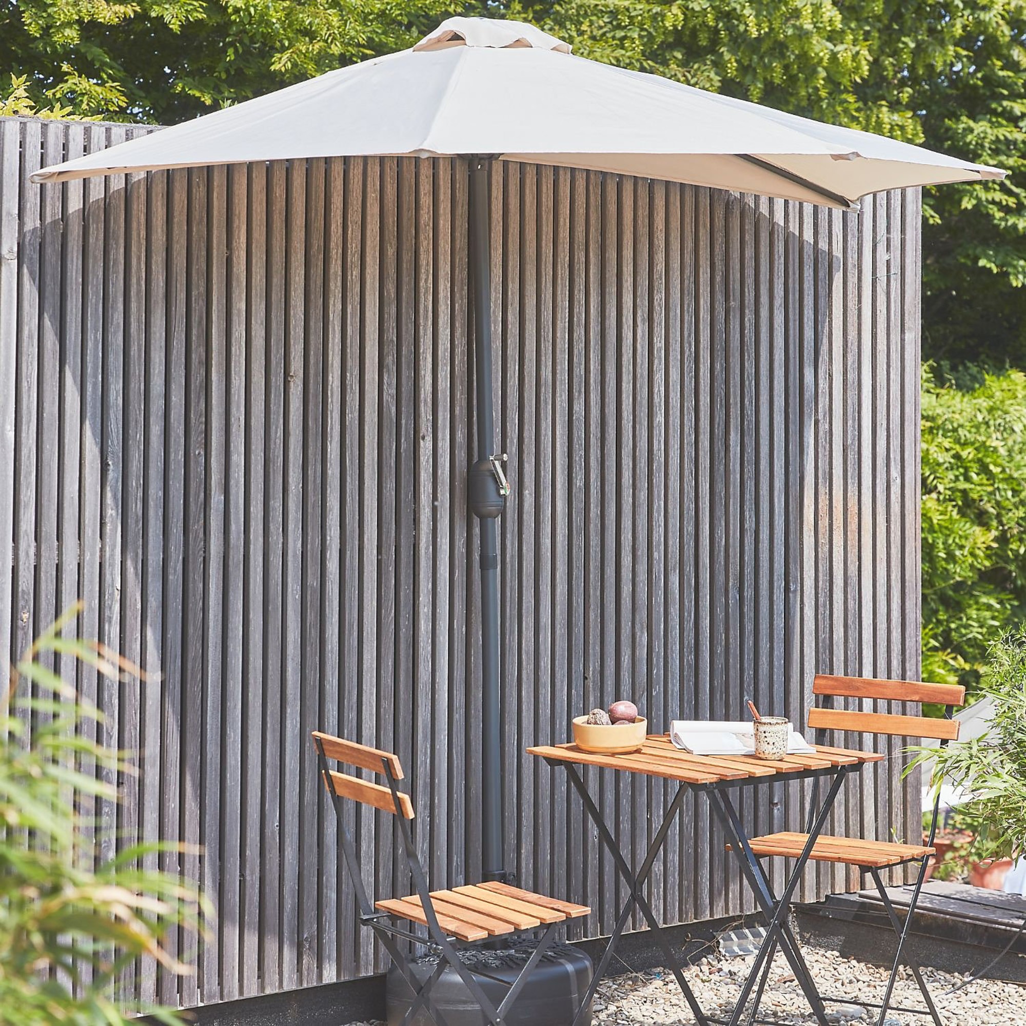 Sweeek half parasol against a panelled wall in a garden next to a wooden bistro set
