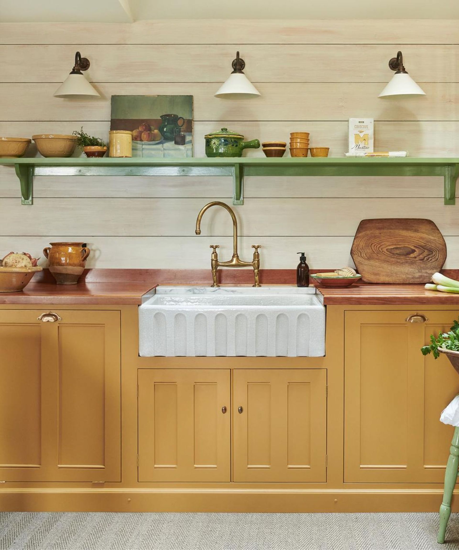 yellow kitchen by devol with wooden countertop and a fluted butler sink with shiplapped walls and a green wooden shelf styled with vintage decor