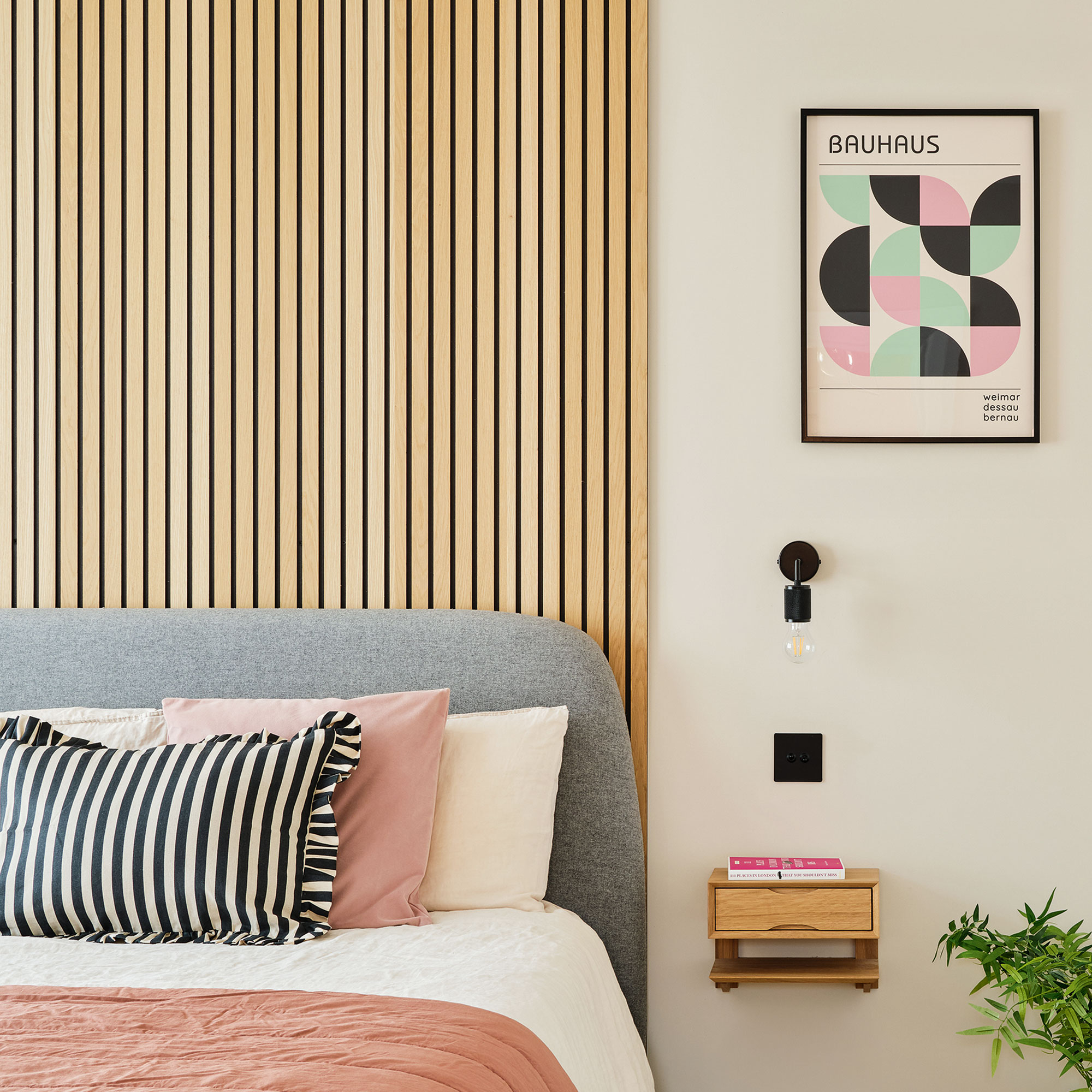 White bedroom with wall panelling behind a grey headboard and a wall mounted side table