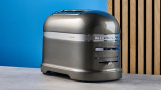 A photograph of the KitchenAid Pro Line toaster on a stone work surface with a blue and wooden background