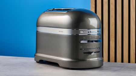 A photograph of the KitchenAid Pro Line toaster on a stone work surface with a blue and wooden background
