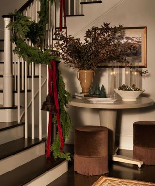 Faux Cedar Pine Garland on a banister beside a side table and a vase filled with autumnal flowers.