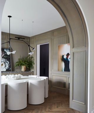 A dining room with a wooden arched entryway and modern white chairs