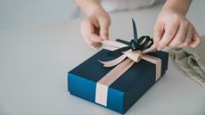 A woman takes apart a pink bow on a present wrapped in blue paper