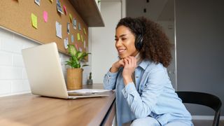 Woman sitting in front of laptop wearing headphones and smiling