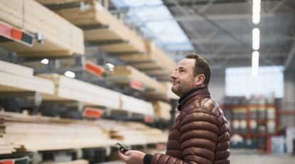 Man looks at wooden planks on shelves in hardware store warehouse.