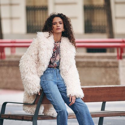 Relaxed woman wearing warm fluffy coat, blouse and jeans from the Next AW collection