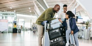 happy family, two parents and two children, with luggage in a sunny airport terminal