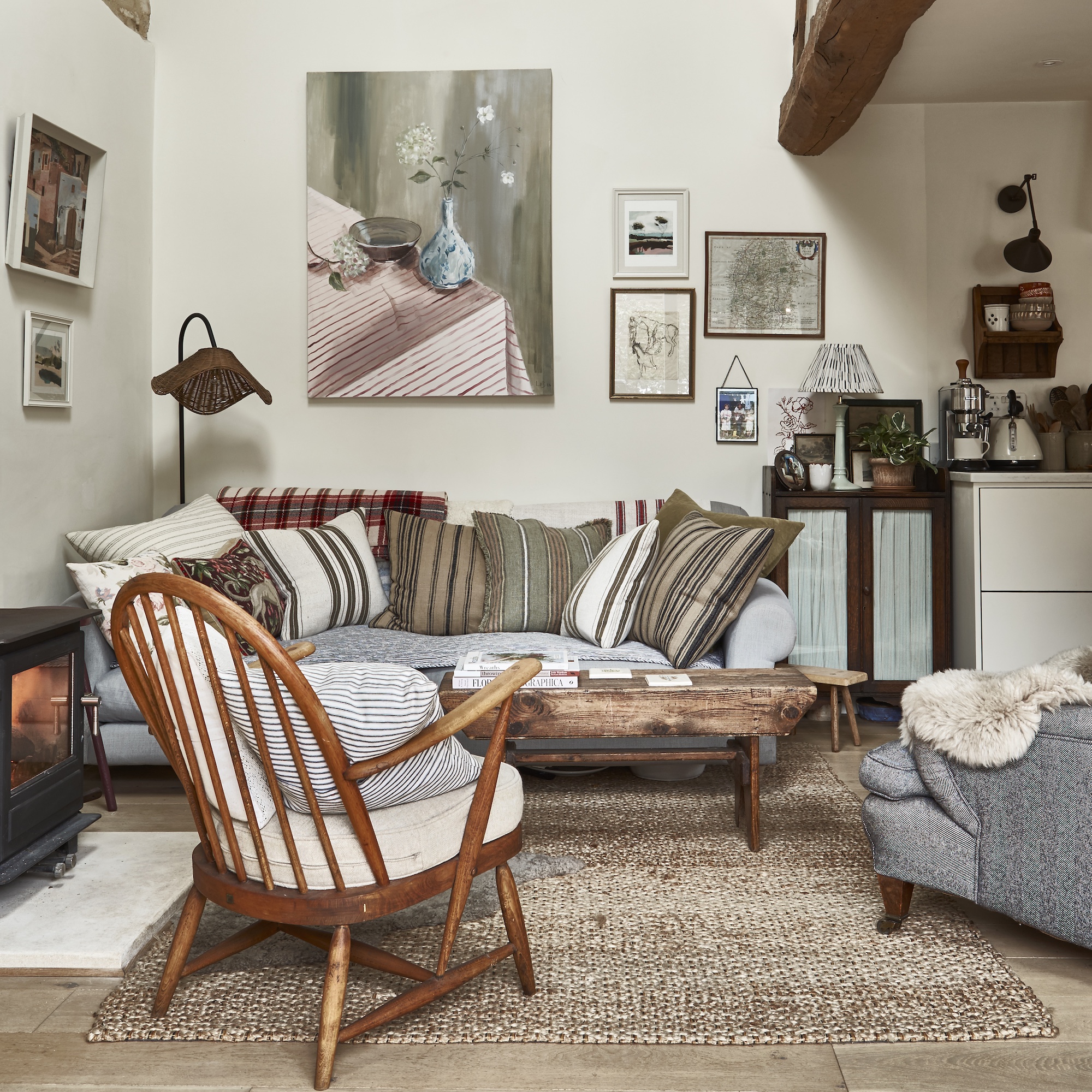 wooden framed archair and sofa with striped cushions beneath a wall of paintings in small cream living room