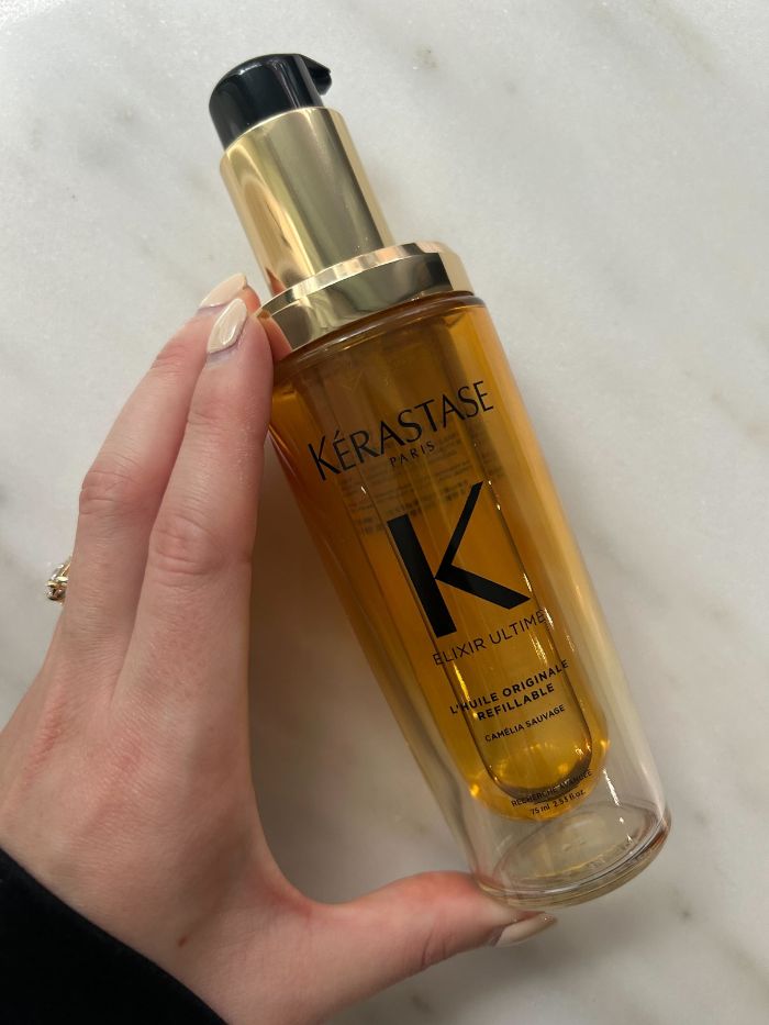 Junior beauty editor Grace Lindsay holding the Kérastase Elixir Ultime Hair Oil on a marble background
