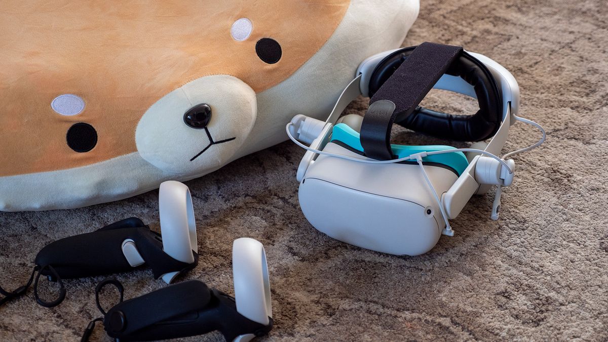 A Meta Quest 2 headset with its controllers and a KIWI Design Comfort battery audio strap next to a doge plushie