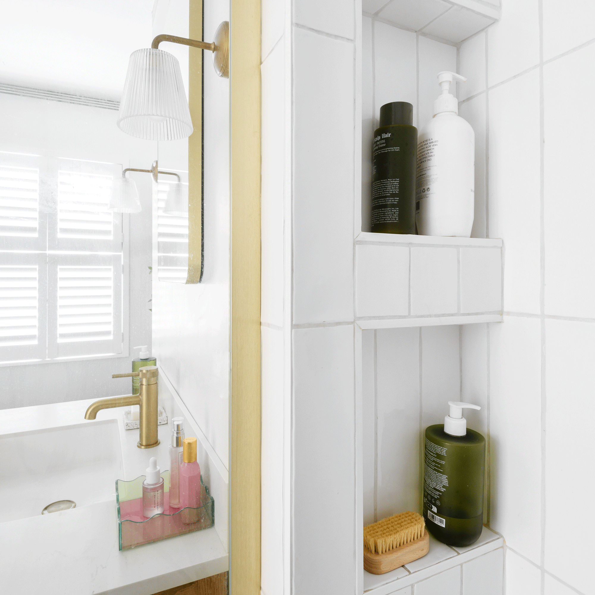 a shower area with recessed shelving overlooking a sink and window with shutters