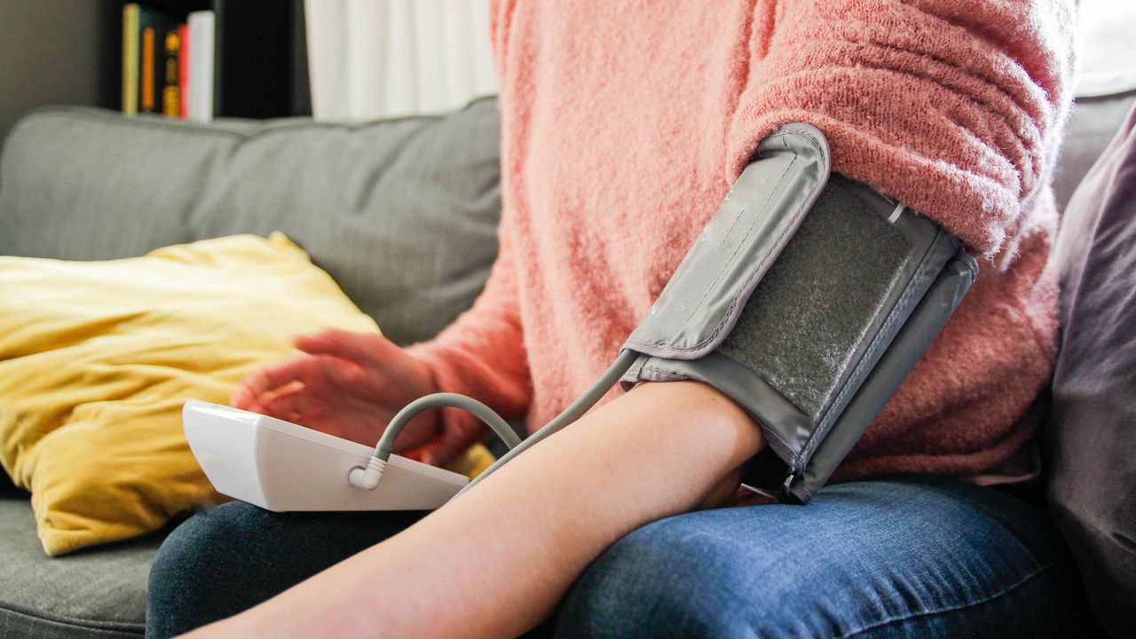 Woman sitting on sofa using machine to check blood pressure