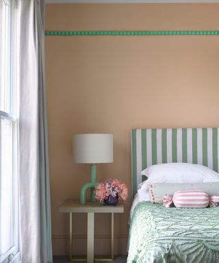 A bedroom with a green bed, wooden table, and pink wall