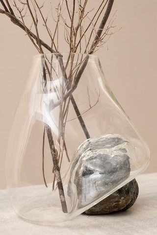 A clear glass vase that's blown around the rock in brown tones. There are tree branches in the vase.