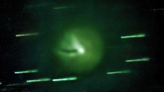 A close up of a green comet with a shadow in its coma