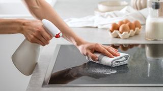 Someone cleaning a a glass stove top with a sponge and soap