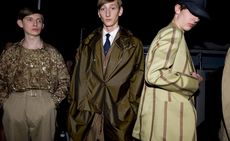 Guys wearing E Tauts S/S 2015 collection. The guy on the left is wearing a brown coloured shirt with matching jacket and wide brown pants. The guy in the middle is wearing a white shirt, navy tie, brown striped jacket and brown overcoat and the guy on the right is wearing a brown striped green jacket