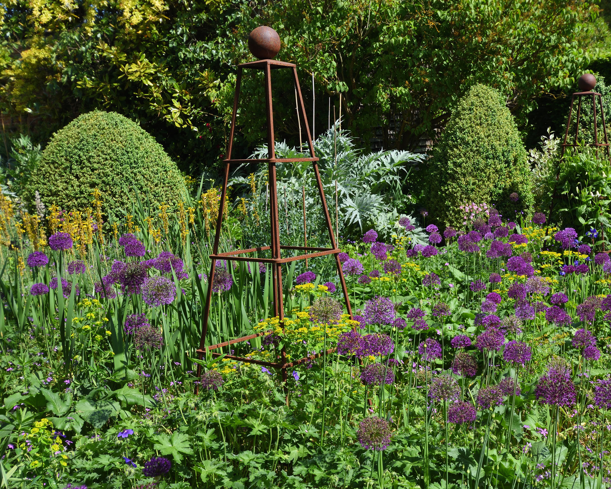 classic garden border with obelisks, topiary and purple allium