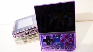 Photo taken by writer Rosalie Newcombe of the Atomic Purple model of the Miyoo Mini Plus handheld, with two transparent Game Boys in the background.