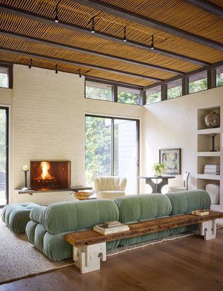 A living space with a teal bubble-shaped Mario Bellini sofa, white brick walls, and a fireplace