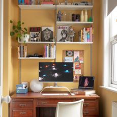 A mustard yellow-painted home office with an IKEA monitor stand on the desk and a computer monitor on top