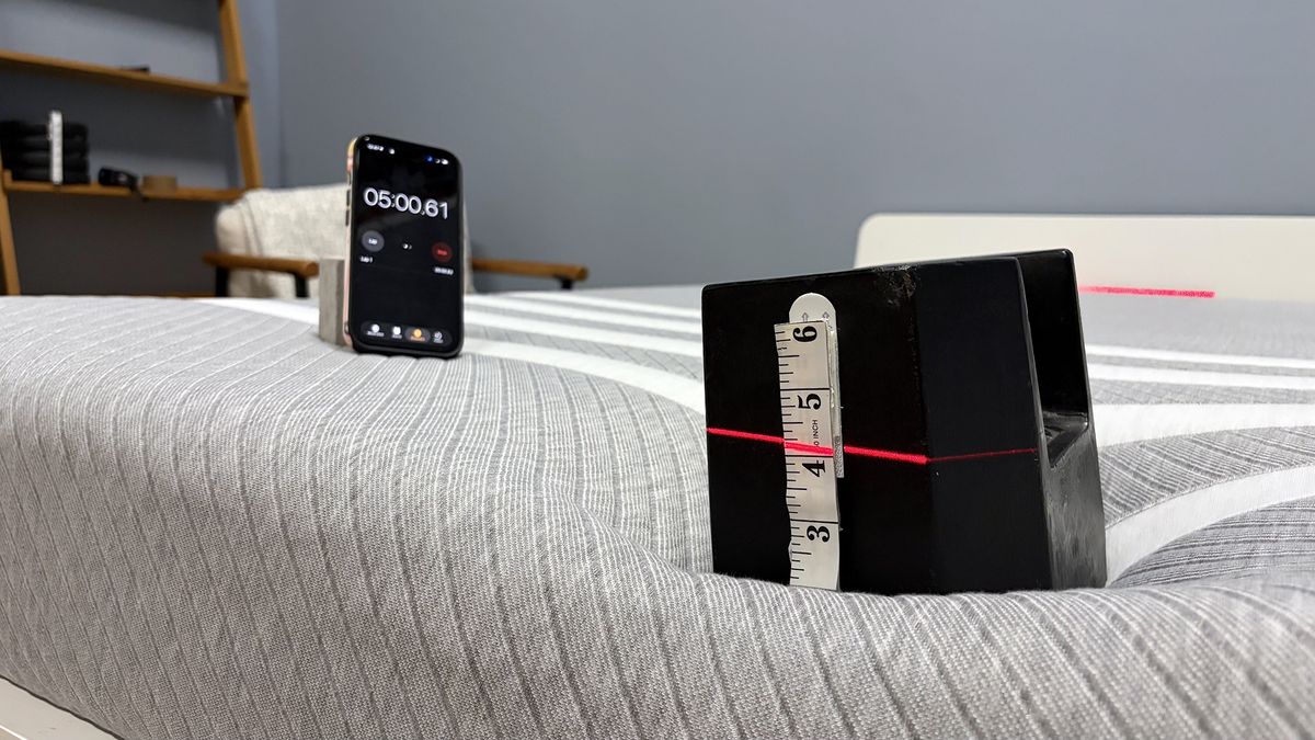 A close up of a 25kg weight balancing on the end of the Leesa mattress, a red laser line cutting through it indicates how far the weight has sank. To the left is a phone showing a five minute timer