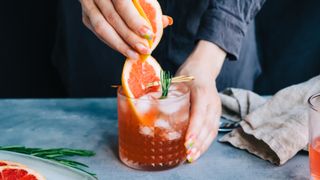 Female bartender hand squeezes juice from fresh grapefruit