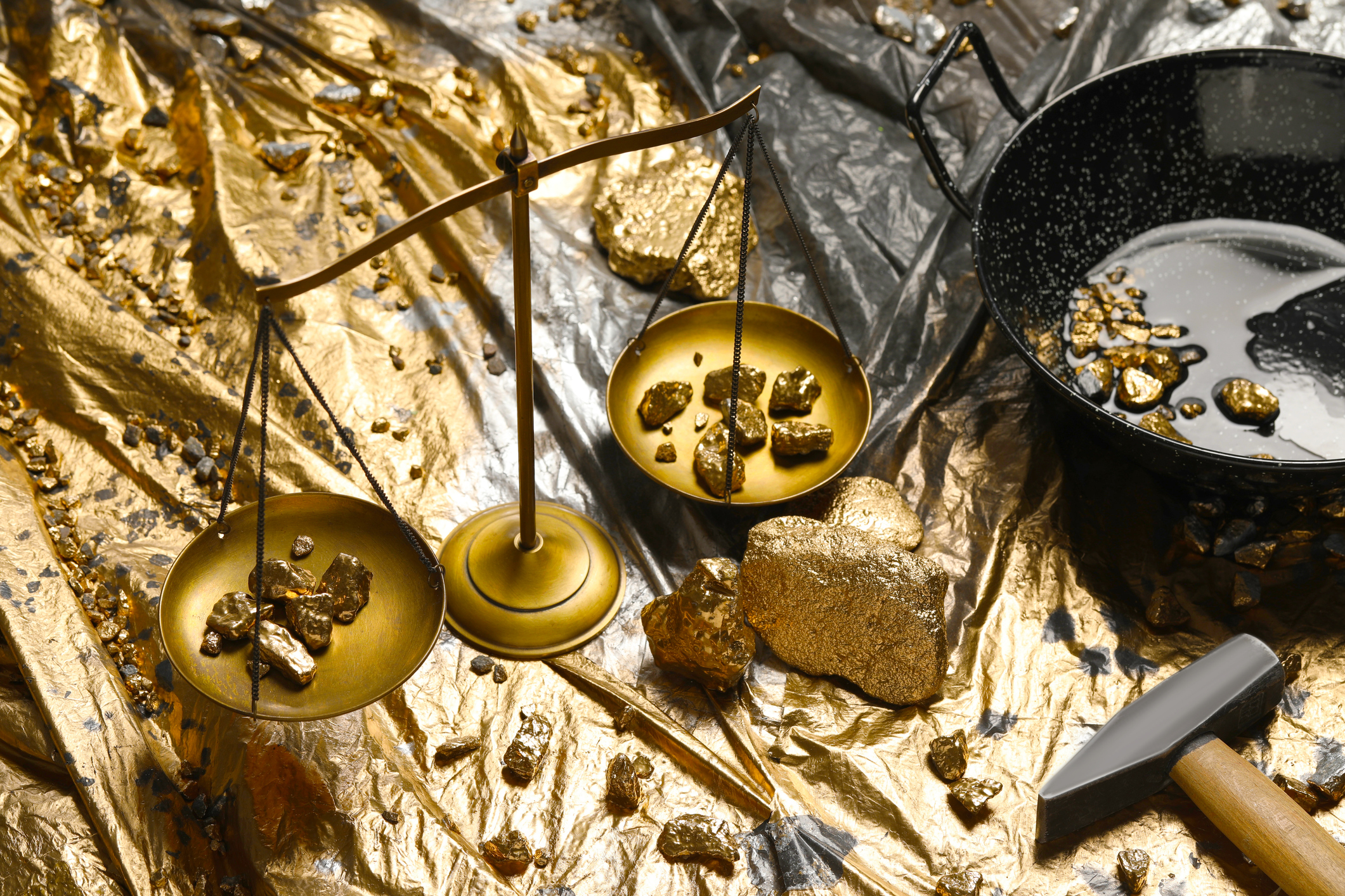 Gold nuggets, vintage scales, hammer and wok on plastic stretch wrap