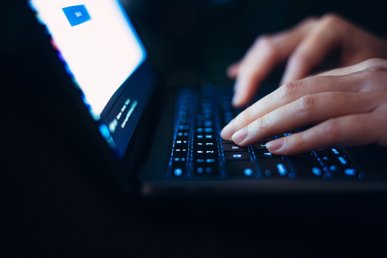 Close up hands of female using laptop in the dark at night, logging in to her online banking account to manage banking and financial bills.