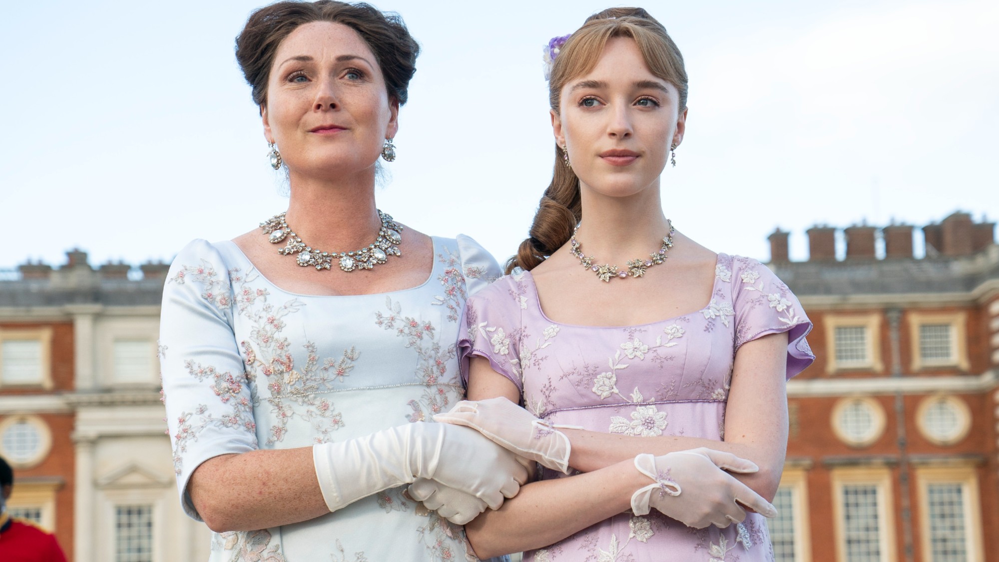 (L to R) Ruth Gemmell as Lady Violet Bridgerton, Phoebe Dyvenor as Daphne Basset walking arm in arm.