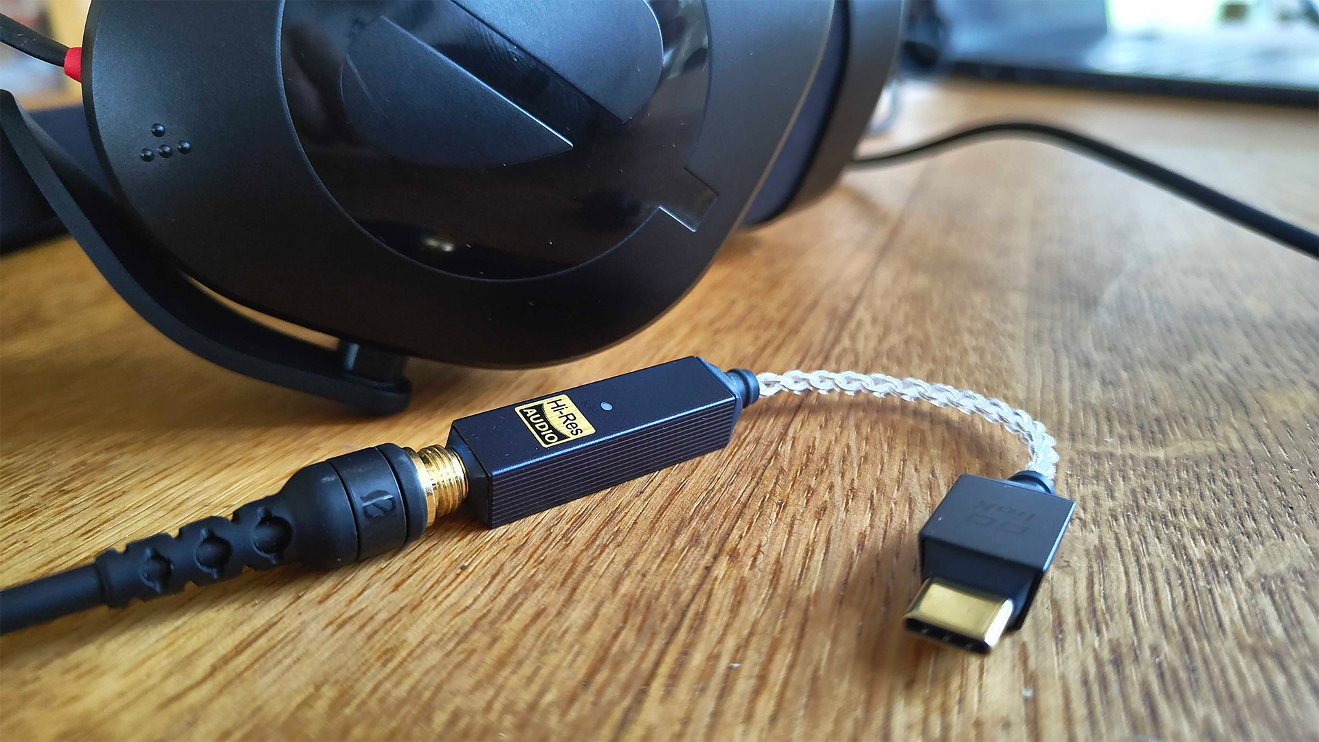iFi Go Link 2 DAC on wooden table top connected to over-ear headphones