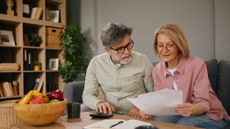 An older couple work on financial paperwork at their kitchen table. 