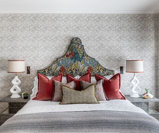 A rococo-inspired headboard has been upholstered in an embroidered cotton satin fabric that depicts dense foliage.
