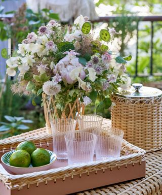 A bar setup on an outdoor ottoman, with limes, an ice bucket, and a floral arrangement