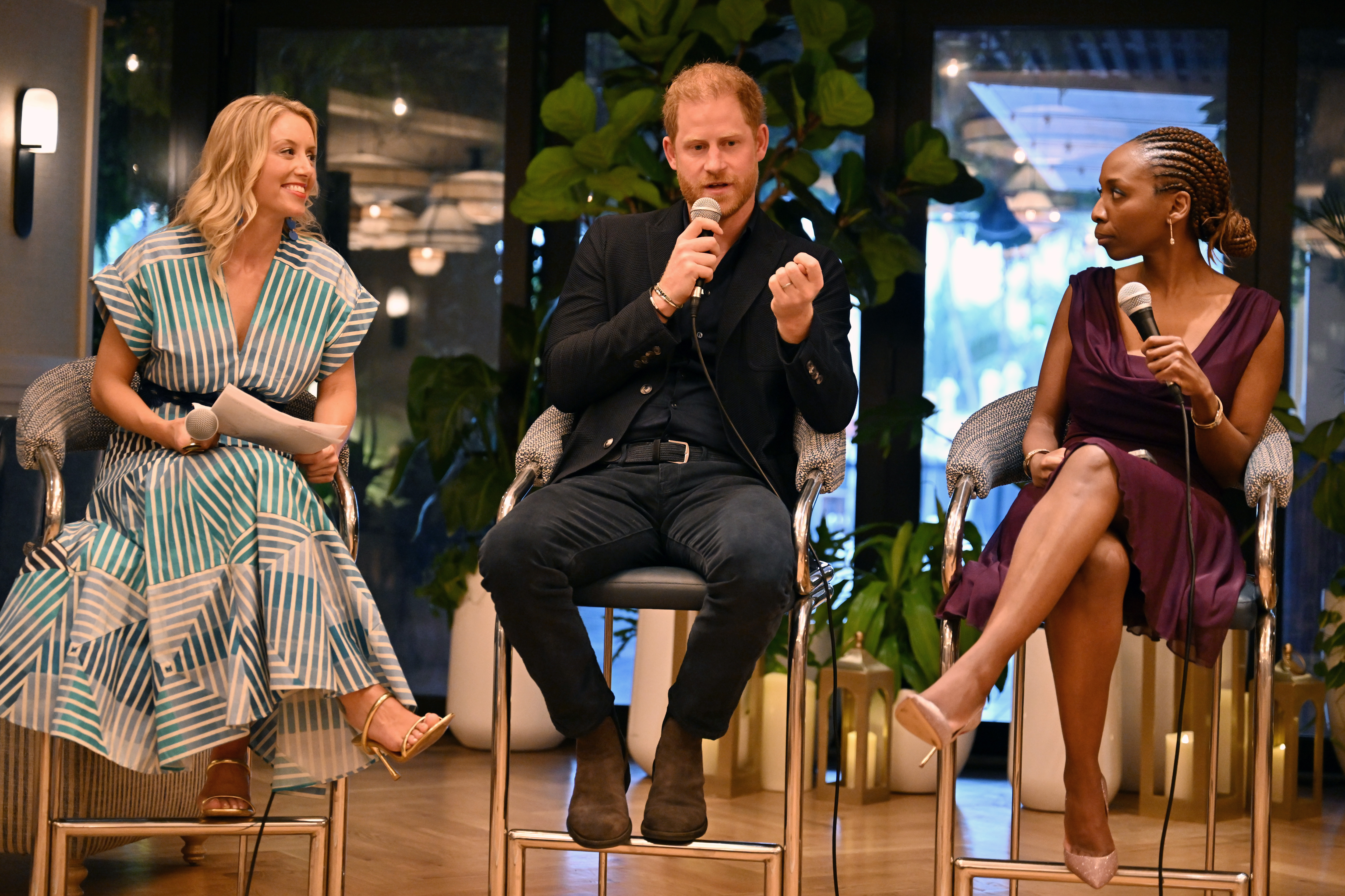 Prince Harry sitting on a chair on stage talking into a mic in between two women