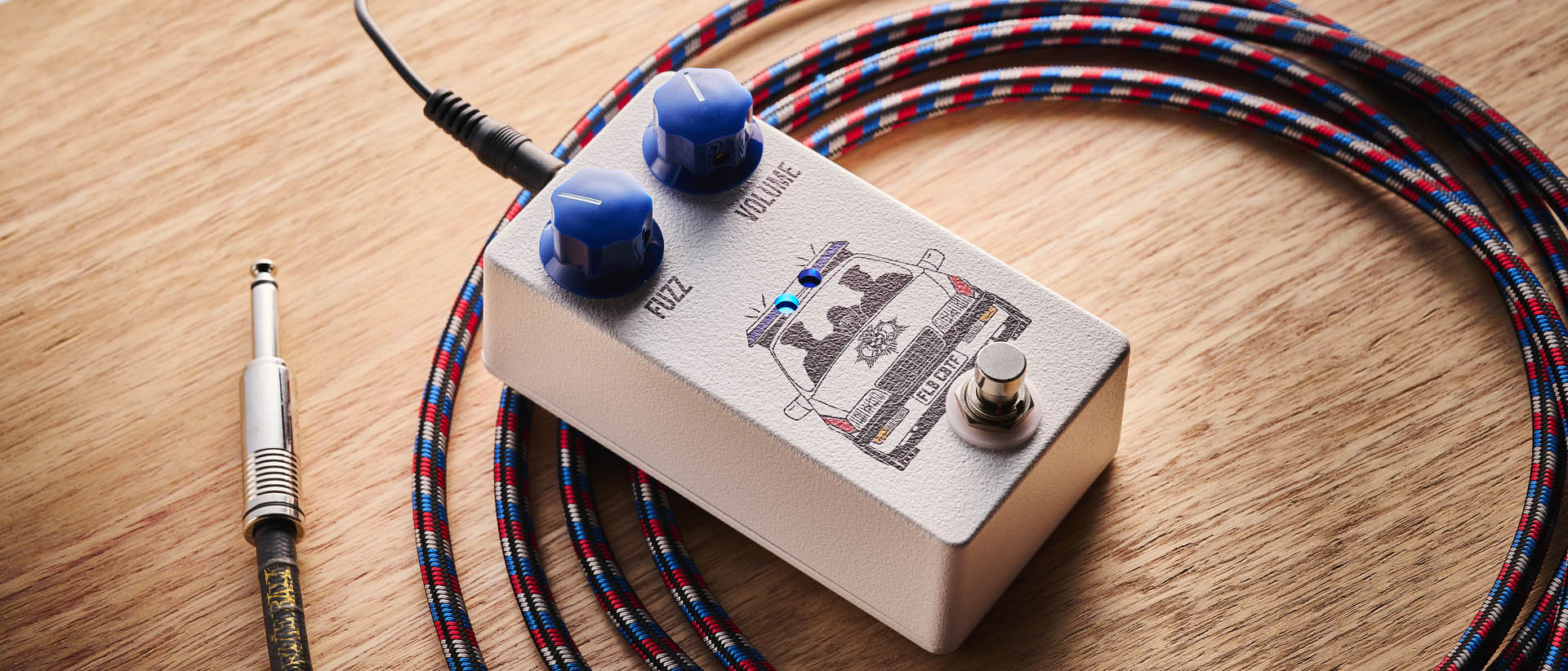 Funny Little Boxes Caught By The Fuzz: inspired by Supergrass, this two-knob fuzz has a white enclosure, blue dials, and a comic graphic of someone being apprehended in a police car.