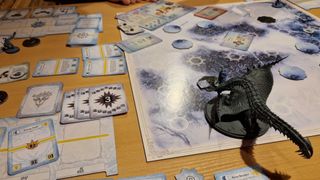 An overview of the Monster Hunter World Iceborne: The Board Game board, tokens, miniatures, and cards on a wooden table