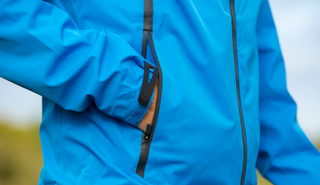 A golfer puts his hands in the pocket of the Ping Taran 3L Rainwear Jacket