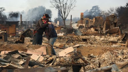 A man and woman hug among the ruins of a home after a wildfire.