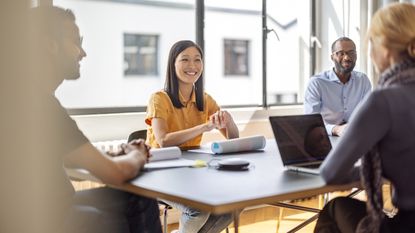People sitting at a table in a conference room smile at one another during a workshop.