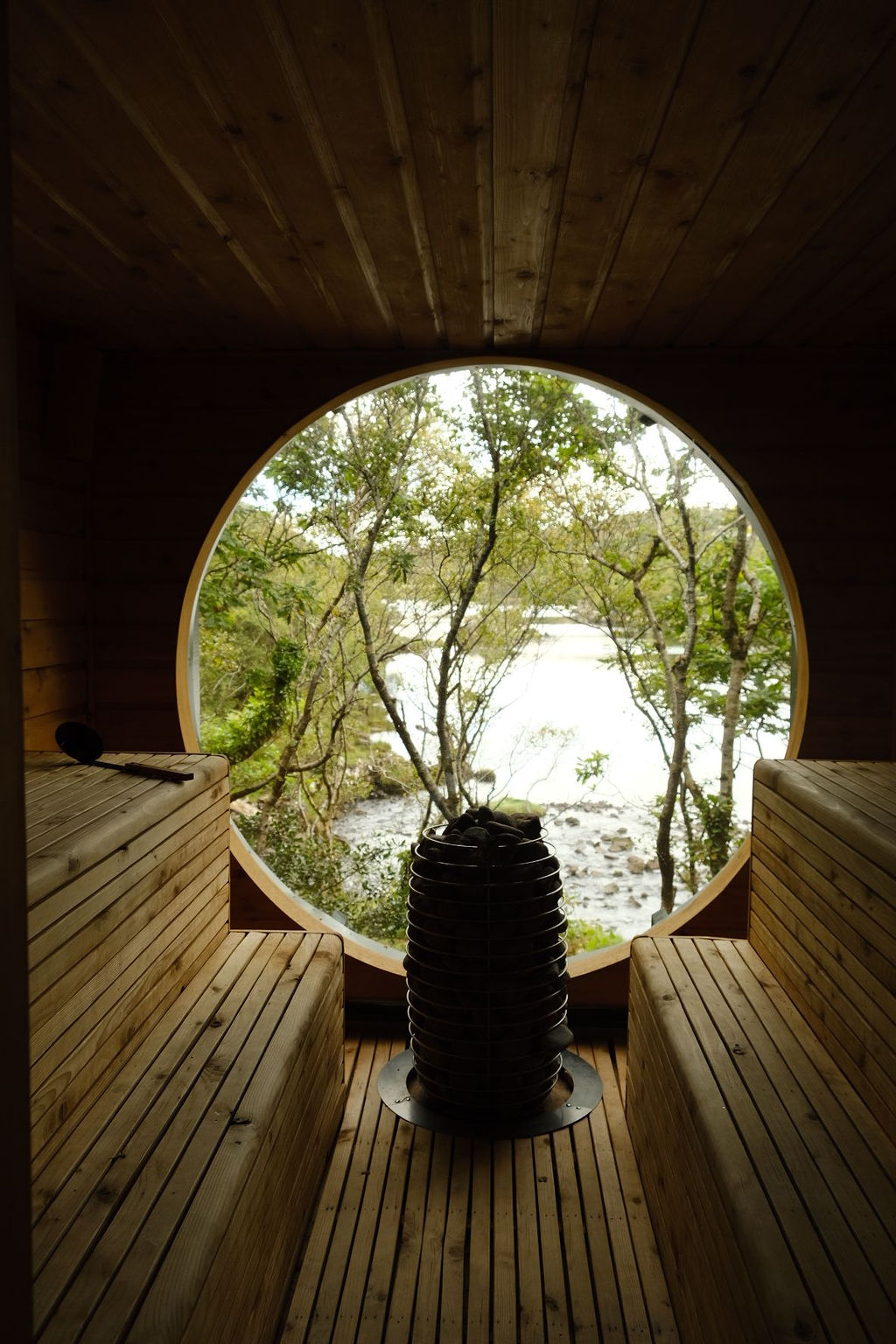 A greenery-immersed, architectural sauna boasts a porthole window that lets guests peek into nature while indoors, and the other way around.