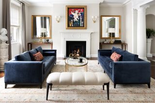 A living room with blue couches, a white ottoman and a muted scheme