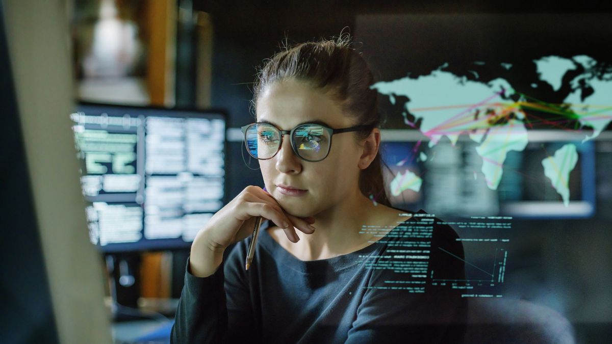 A woman in a dark office looking at multiple computer monitors displaying data analysis tools