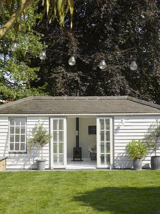 white timber clad garden room with large lawn and potted plants